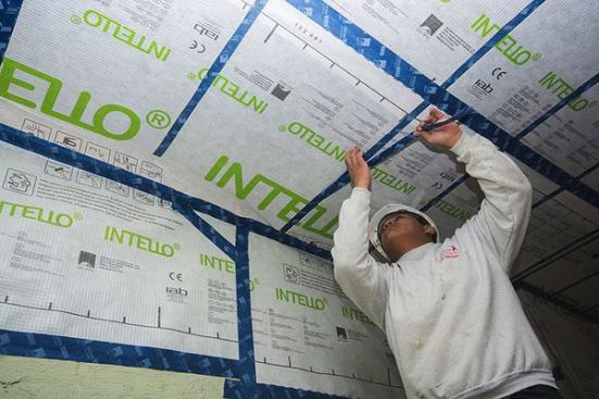 A carpenter applies ProClima Tescon Vana tape to the Intello smart vapor control membrane along the line of the framing member. Passive House consultant Cramer Silkworth explains: “Generally, you don't have to tape over the fasteners for air-tightness. In this case, after tacking the Intello in place, the guys are taping the staple path first, then stapling through both the tape and the Intello to reinforce it there, but only as an extra precaution. Often, we apply cross-strapping to a ceiling before applying drywall, to form a service cavity for wiring, and that would help hold the cellulose up. But in this case, we have a lower ceiling, so we just want a bit of insurance.”