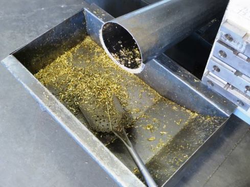 Bronze chips and shavings collect in a bin at the base of a CNC machine.