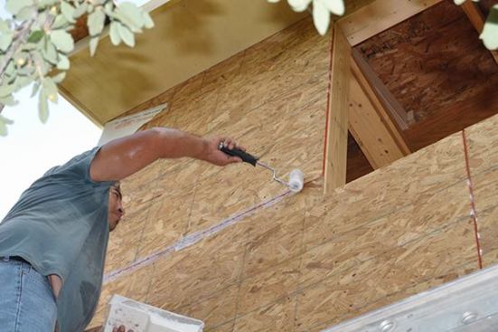 Carpenter using a mini-roller to apply the Dockskin primer to the OSB seams prior to taping.