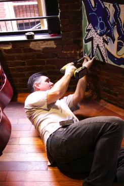 A crew member screws into the mortar joint of the brick wall to secure a “REVRB” panel in place.