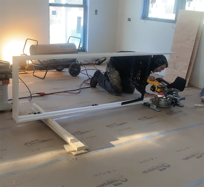 You may need to cut the jamb down in length before standing the unit in the rough opening for scribing. The author makes his jamb cuts using a miter saw on the floor. Without the door, the jamb legs will flop around, so he may attach a temporary stretcher 12 inches up from the bottom of the unit. In the photo above, he uses a framing square as a stretcher—a fast solution that works for a 2'-0" door.