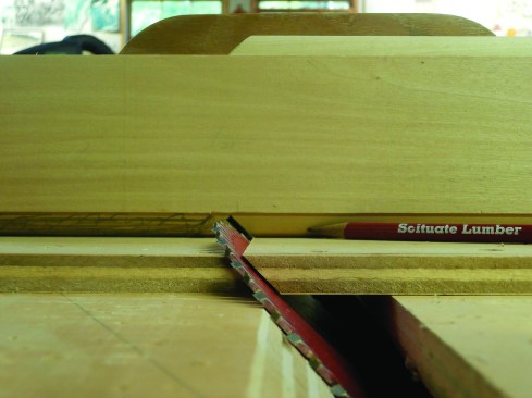 Making the initial cut for the jack miters is the trickiest part. He uses a plywood sliding table to crosscut the miter, doing a test cut on a piece of poplar to get the depth exact before making a finish cut on the mahogany.