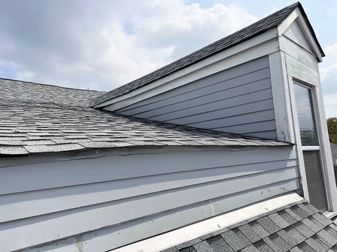 No cut back or step flashing. Siding running down to the roof shingles is wicking water and is at risk of failing. Worse, this roof also lacks step flashing. The combined errors are causing water leaks inside the dormer.