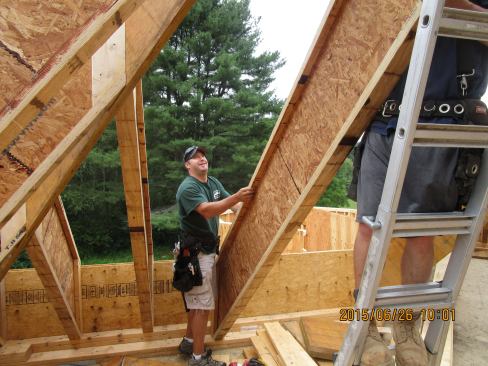 A carpenter positions the foot of a wood I-joist commont rafter during roof framing.