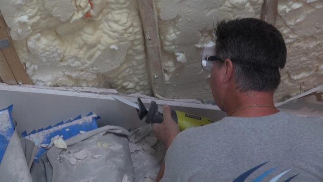The crew trims drywall flush with the stair skirt board using a battery-operated recip saw.