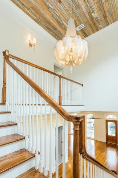 The ceiling at the top of the stairs features reclaimed bead board that was taken from various places inside the home. It was then stripped and left exposed to give it a distressed look. A Victorian-style chandelier with brushed nickel offers a modern vibe while still reflecting on the past.