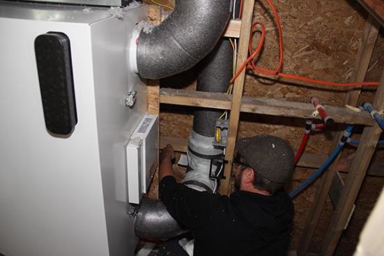 Placetailor project manager Travis Anderson uses Siga tape to sel an outdoor air intake line for the Air Pohoda energy recovery ventilator at the Roxbury, Mass., “Supply House” job. Placetailor crafted a mix-and-match hybrid system for this project: The ERV unit shown is supplied by Air Pohoda, but the air intake and exhaust lines are an insulated expanded polystyrene (EPS) product supplied by Zehnder. Placetailor preferred the Zehnder ducting in this application because of its insulation qualities and its resistance to crushing in the dense-blown cellulose-insulated wall cavity.