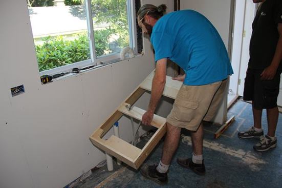 On site, Jeff and Joe set a pre-built toe-kick base over the rough plumbing for the kitchen sink.