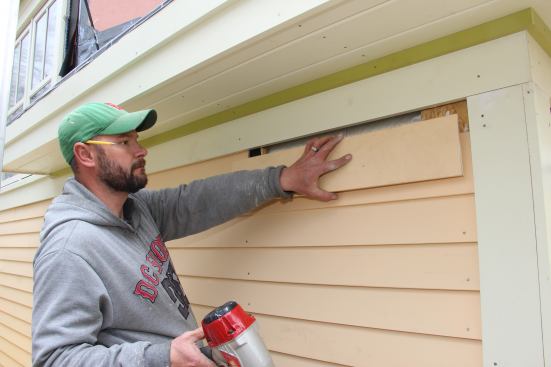 Fenton places the final clapboard at the top of the wall. The carpenters took care to lay out the siding to finish with a full course at the top, where the siding meets the frieze board. This ensures that the thin top edge of the top clapboard will slide up into the gap behind the frieze, leaving a gap between the two pieces for free airflow in and out of the rain screen drainage gap.