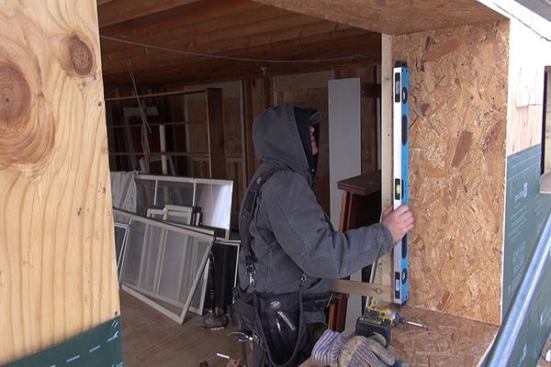 EcoCor carpenter Rich Perry builds a window extension buck assembly onto an existing window in the Newcastle “Ripple” house. The window bucks extend out to the plane created by the wood I-joists applied to the house exterior, and will have to be integrated into the air control layer in the center of the wall, as well as into the drainage plane layer at the wall’s outboard face. High-performance windows will later be installed into the “punched opening” created by the OSB bucks.
