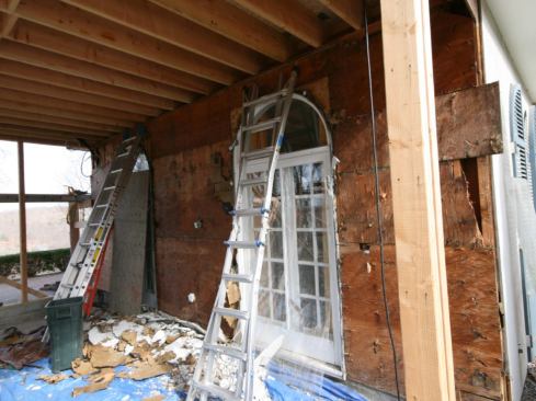 We then turned our attention to the gable-end wall of the main house. At the bottom, the cladding extended down into the space that would be occupied by the slab, so we decided to complete all of the demo first. After laying tarps on the slab fill to catch the debris, we stripped the wall down to the studs, removing the three-coat stucco, metal lath, building paper, plywood sheathing, and fiberglass batt insulation. We then poured the slab used 4,000-psi concrete with welded wire mat reinforcing. After it was poured, it needed to cure for at least 28 days before we could begin installing the radiant tile floor.