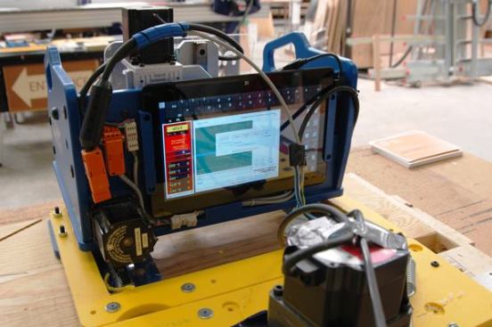 The Handibot is controlled via the user’s tablet computer which is carried onboard when the machine is in motion. The latest build of the Handibot has the tablet slot located on the front of the unit for easier access (instead of on the back as shown). In the future, the tool will also be able to be controlled wirelessly with a variety of devices.