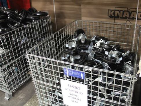 Parts such as wheels, handles, and latch hardware are stored in metal bins near assembly areas.