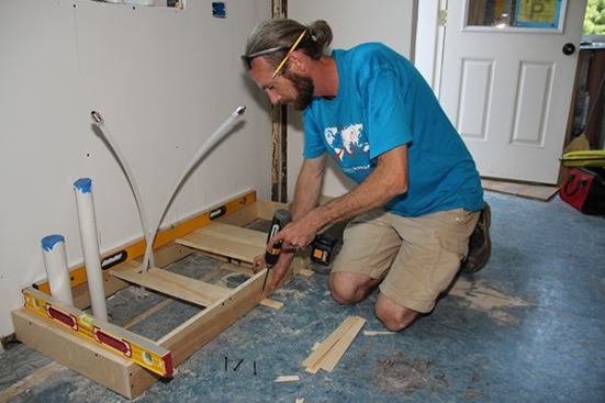 With the toe-kick base shimmed and leveled to his satisfaction, Jeff sends a screw home through the pre-drilled pocket hole, through the shim, and into the existing subfloor.
