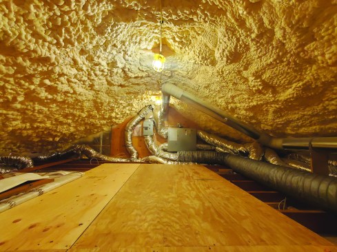 The author moved insulation from the attic floor to the roof plane, allowing mechanicals and ducting to remain inside the building envelope. First, a 1-inch air gap below the roof sheathing was created using strips of plywood as spacers and 1-inch XPS foam between the rafters topped with 12 inches of open-cell foam, for a combined R-value of around 50.
