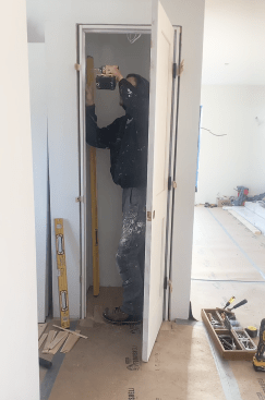 After hanging the door, he aligns the latch side, keeping an even reveal (the gap between the door and the jamb). He first secures the top of the jamb. He checks to be sure the door hits the stop evenly, then secures the bottom, and finally shims behind the strike plate until the gap is correct.