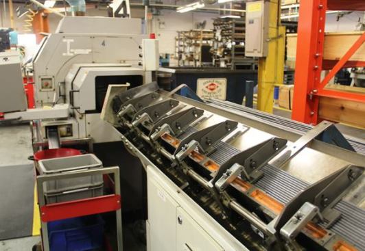 This CNC lathe is making screwdriver blades from steel bar stock. The stock feeds in from the right; the lathe is machine with the number “4” on it.