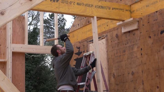 Hill drives a temporary support post into position under the beam, so he can remove the temporary shelf from the wall under the beam and install a permanent Simpson structural hanger.