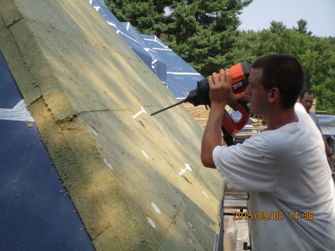 The Auburndale team is attaching Roxul rock wool insulation to the walls and roof of the house using a system supplied by Ramset. Here, a carpenter prepares to insert the long driver pin into the hollow fastener tube.