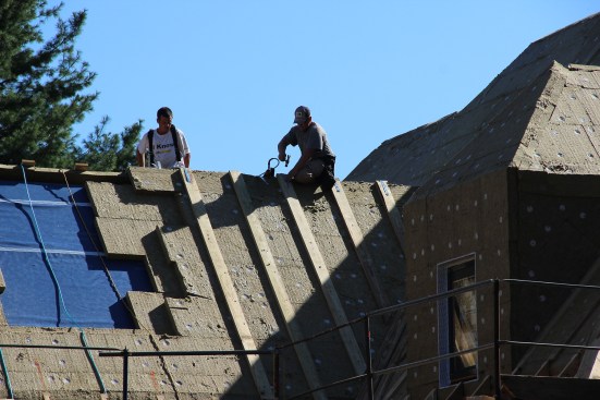 Framers apply vertical 2x6 strapping over the Roxul rock wool insulation, to create an air channel under what will be the sheathing for a slate roof. The uninsulated portion of roof at left will be the location for a skylight.