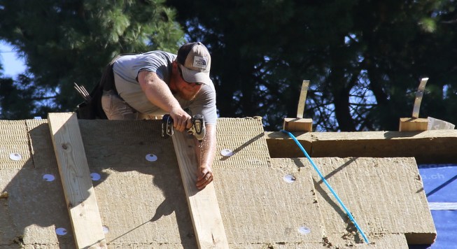 A framer uses long GRK structural screws to attach 2x6 strapping for the structural deck for a slate roof.