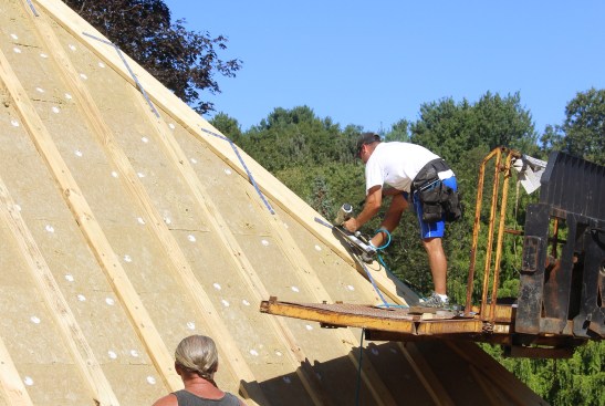 A framer installs metal strapping across the 2x strapping at the roof hip, to strengthen the roof against wind uplift loads.