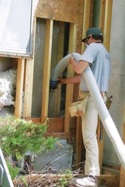 A worker vacuums failed cellulose insulation out of a double stud-wall cavity after an energy audit revealed major settling and pest infestation.