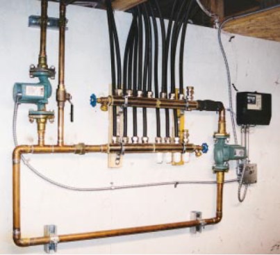 The manifold loop is installed in a mechanical room where it is easily accessed. The injection pump is at left, above the closely spaced tees. Halfinch PEX-AL-PEX circuits begin and end at the manifolds. The supply manifold is on top. The system control and manifold circulator are at far right.