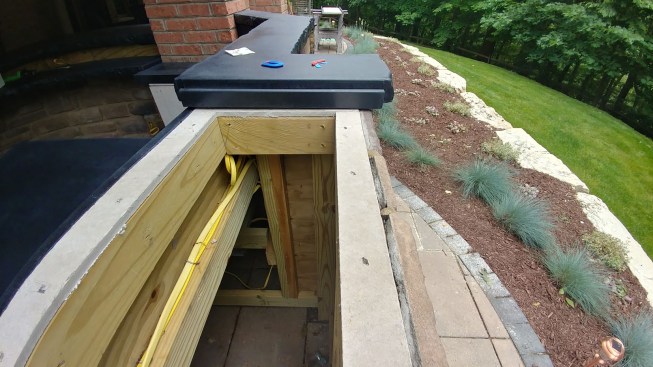 To install a pop-up style of TV lift in an outdoor bar, the author devised a simple gutter (shown here at one end  where the concrete counter ends at the opening for the TV and pop-up assembly) to channel water away from the assembly.