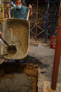 A worker pours concrete from a wheelbarrow into the hole in the slab.