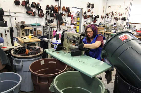 A seamster—the gender neutral term for one who sews professionally—folds and stitches the main body of a pouch that will be attached to a tool belt. Behind her (on the wall) are samples of everything the company makes, which are there for reference.