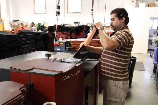 This machine operator feeds pre-cut leather through a $30,000 splitter to shave off any high spots, because variations in thickness (which are multiplied when leather is folded or layered) make it harder to do a good job stitching and riveting.