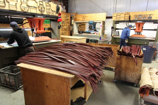 These "suspender" straps were cut from slightly larger strips of leather using one of the die cutting presses in the background. Note the many dies that are stored on or near the machines in this room.