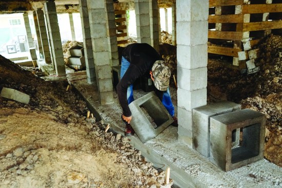 The crew member readies the heavy 16-inch-square block for constructing the column. Once the blocks are stacked and mortared in place, the pier will be fully grouted to create a solid masonry column.