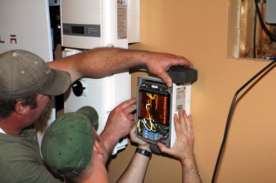 Holding the transformer in place, Millette and Ritz trace the location on the wall. In service, the automatic transformer will balance the voltage and create a neutral when backed-up circuits running off battery power. The transformer enables the system to supply a consistent 120 volts to backed-up circuits, explained Millette. Without it, circuits would only have 240v and the power would fluctuate.