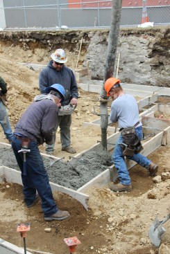 Concrete masons with JB Concrete Construction (Bridgton, Maine) wrestle the pump hose to place footings on a tight site in Portland, Maine, as the pump truck operator controls the flow on concrete using a remote control.