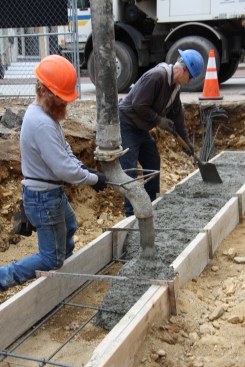 Masons place concrete footings for an infill project. A four-inch slump was specified for the placement, requiring shovel and trowel work to smooth and level the footing surface.