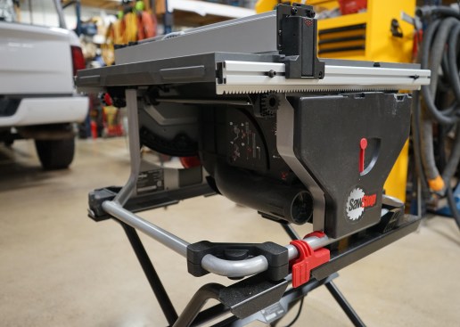 The rack-and-pinion fence on the CTS reliably holds the fence square to the blade.  The red quick release  (in foreground; there is another on the front of the saw diagonally opposite this one) secures the saw housing to the folding stand (available as an added accessory). Note, too, the 2 1/2-inch dust collection port, which pulls from directly under the blade. This configuration noticeably collects dust better than many other compact table saws.