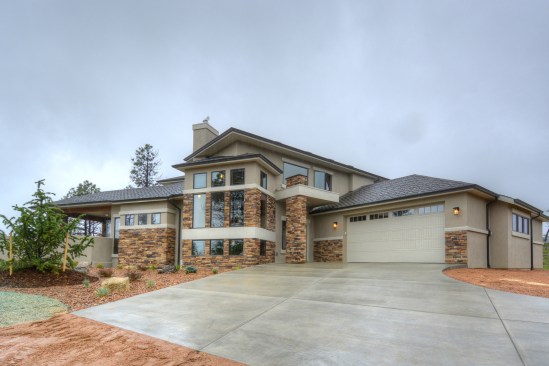 The homes have cultured stone and fiber-cement cladding systems and are set in sparsely planted landscapes with stone mulch.
