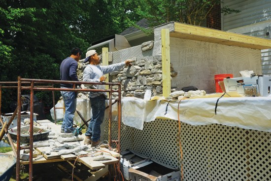 The masons work in sections, back-buttering each stone and pressing it into the scratch coat.