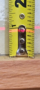 With the laser line indicating the level mark, the tape measure shows that the cabinet must be raised almost 15/16 inch.