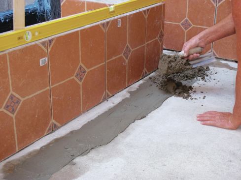 While the Portland cement slurry is still wet, pile on a stiff mortar mixture that's four parts sand to one part cement with just enough water to combine them. Compact the mortar to the correct height and slope by tapping on a 6-foot straightedge laid along the top of the pile.