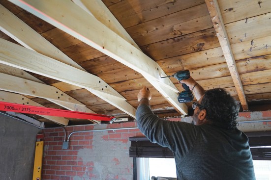 Toby fastens the rafter ties with structural screws. Note the eye hook attached to the top plate of the wall to secure the come-along.