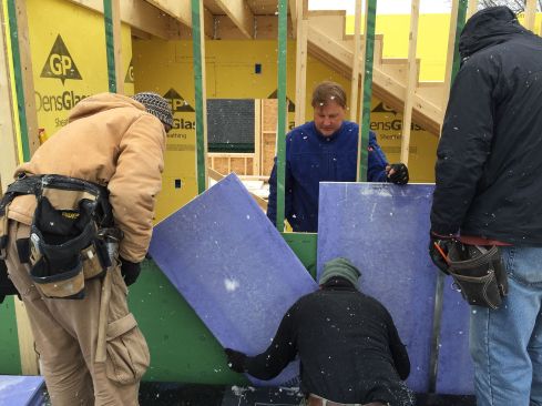 The crew slips gypsum board into the space between the old building and the new frame under construction.