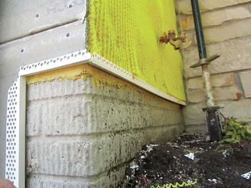 A vinyl J-track, or casing bead, is installed at the base of the wall to receive the base panels. It has weep holes that allow water to drain out, and it functions as a screed when the stucco base coat is troweled on.