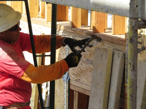 To place the ties, the scaffold erector drives duplex nails partway into the framing, wraps the wire loosely around the scaffold and the nails, then drives the nails home to tighten the wire.