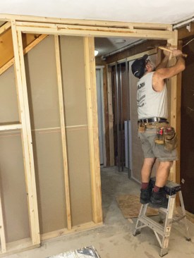 To help locate the frame header brackets, the author partially nailed a flat-head nail into each trimmer on either side of the opening so that the nails were 80 3/4 inches above the finish floor and centered on the trimmers. He left the nail heads proud by about 1/8 inch so that the end brackets of the frame header could slip over the nails.
