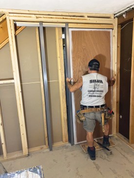 The author also mounted a rubber bumper on the back edge of the door 40 inches from the bottom. He then inserted the wheeled hangers into the track and used a flat bar to lift the heavy door so that the hanger pins engaged the door plates.