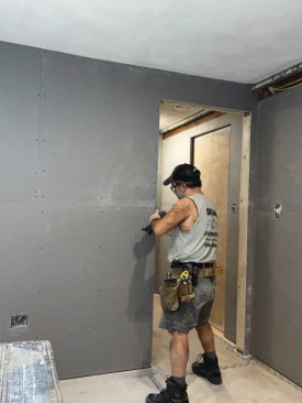 With the pocket door installed in the frame, the author laid down Dricore panels over the concrete slab floor, shimming them as needed to level the floor, then installed 1/2-inch plywood subfloor over the panels, staggering the seams and covering the new subfloor with Ram Board temporary protective floor covering. When installing the drywall, the author used short self-tapping screws to attach the drywall to the steel split studs.
