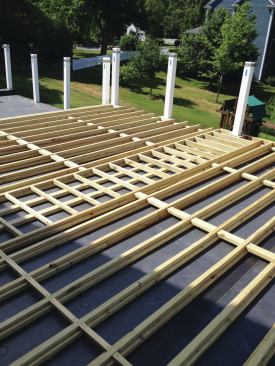 The deck was built along with the garage, not as a retrofit project, which allowed the railing posts to be incorporated into the roof framing. The deck framing consists of sleepers screwed to tapered joists. Note the blocking, which was installed to support the meeting boards that run perpendicular to the field in the center of the upper deck.